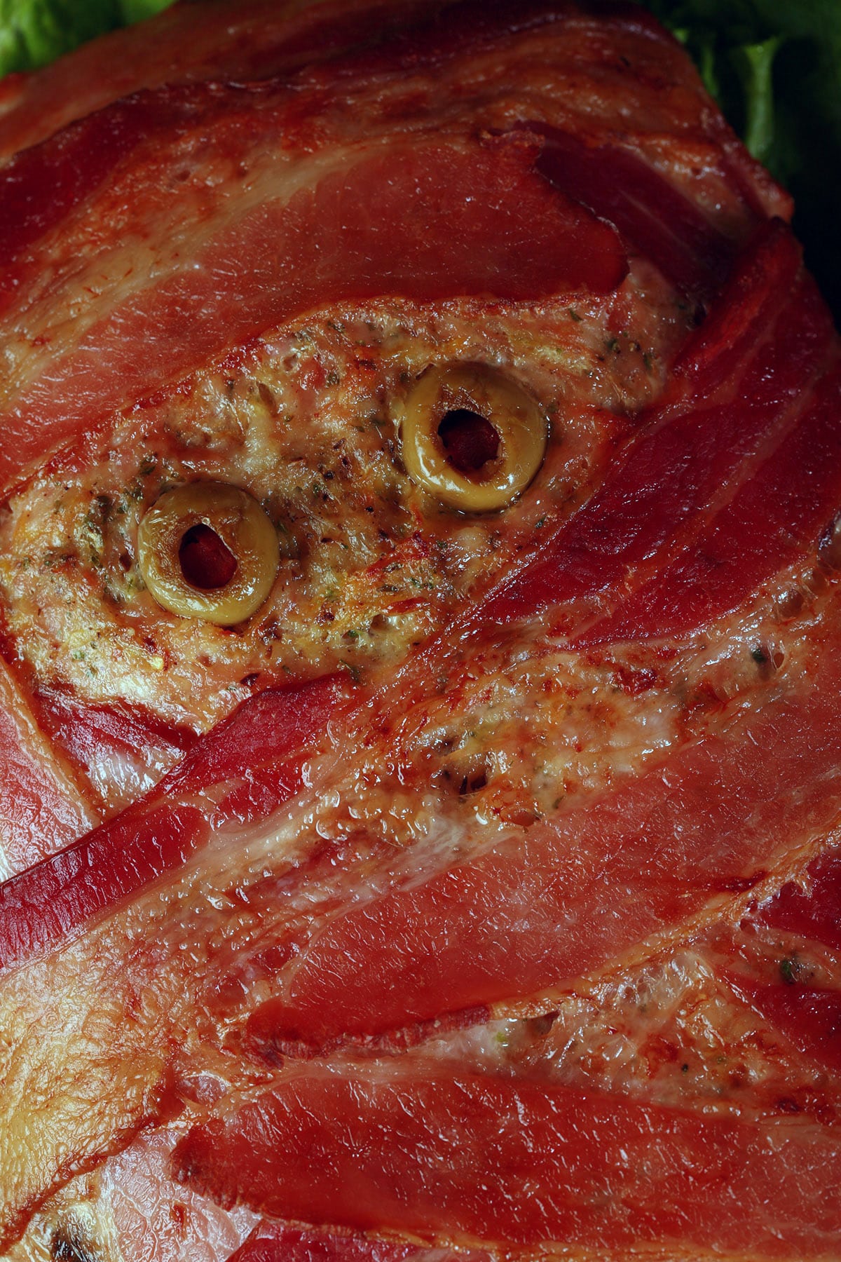 A close up view of a mummy meatloaf. It’s a bacon wrapped meatloaf with olive eyes.