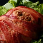 A close up view of a mummy meatloaf. It's a bacon wrapped meatloaf with olive eyes.