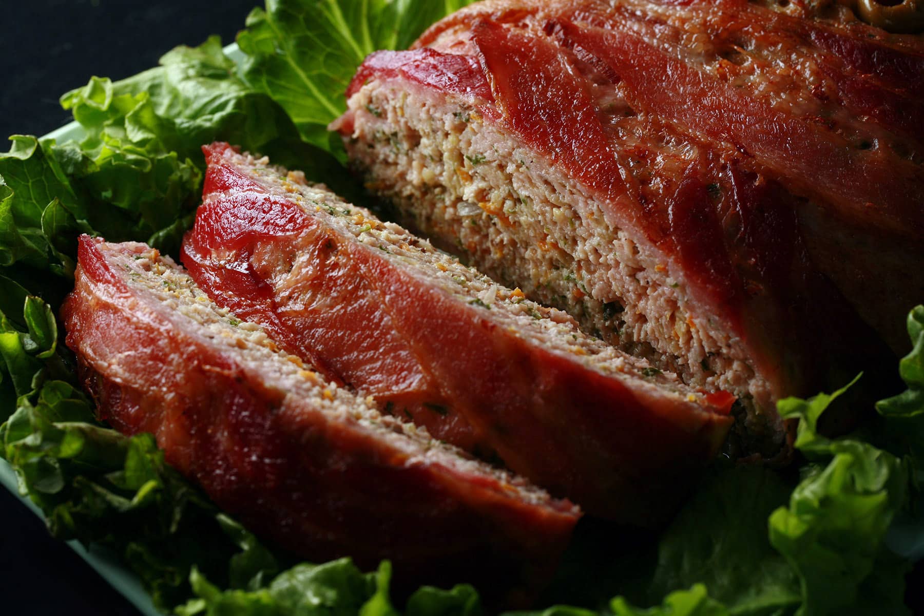 A close up view of a keto bacon wrapped meatloaf.  Shredded veggies are visible.