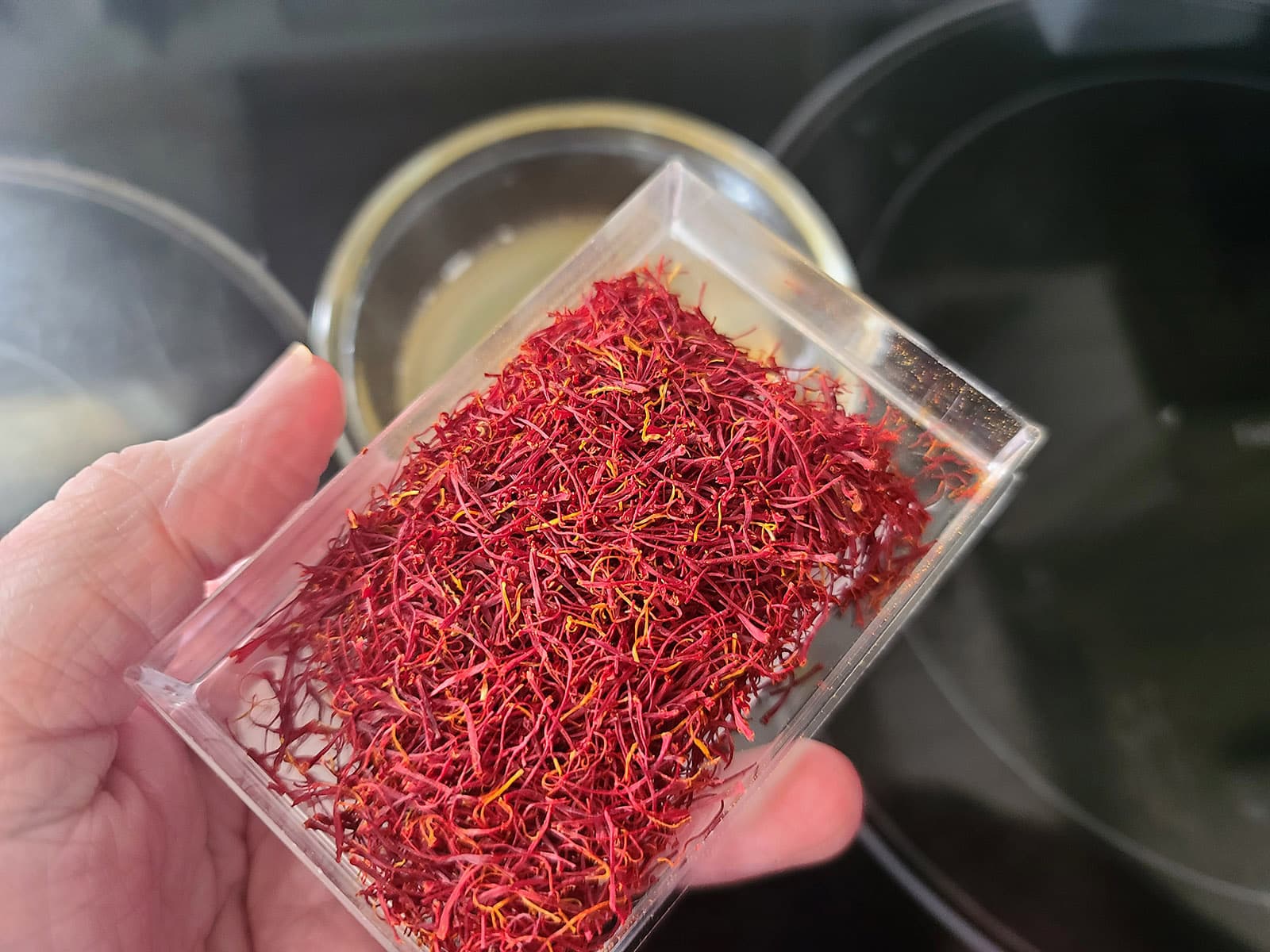 A hand holds up a plastic container of saffron threads.