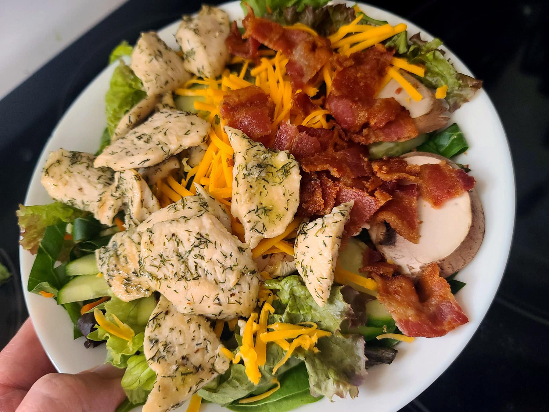 A bowl of salad with chicken and bacon on it.