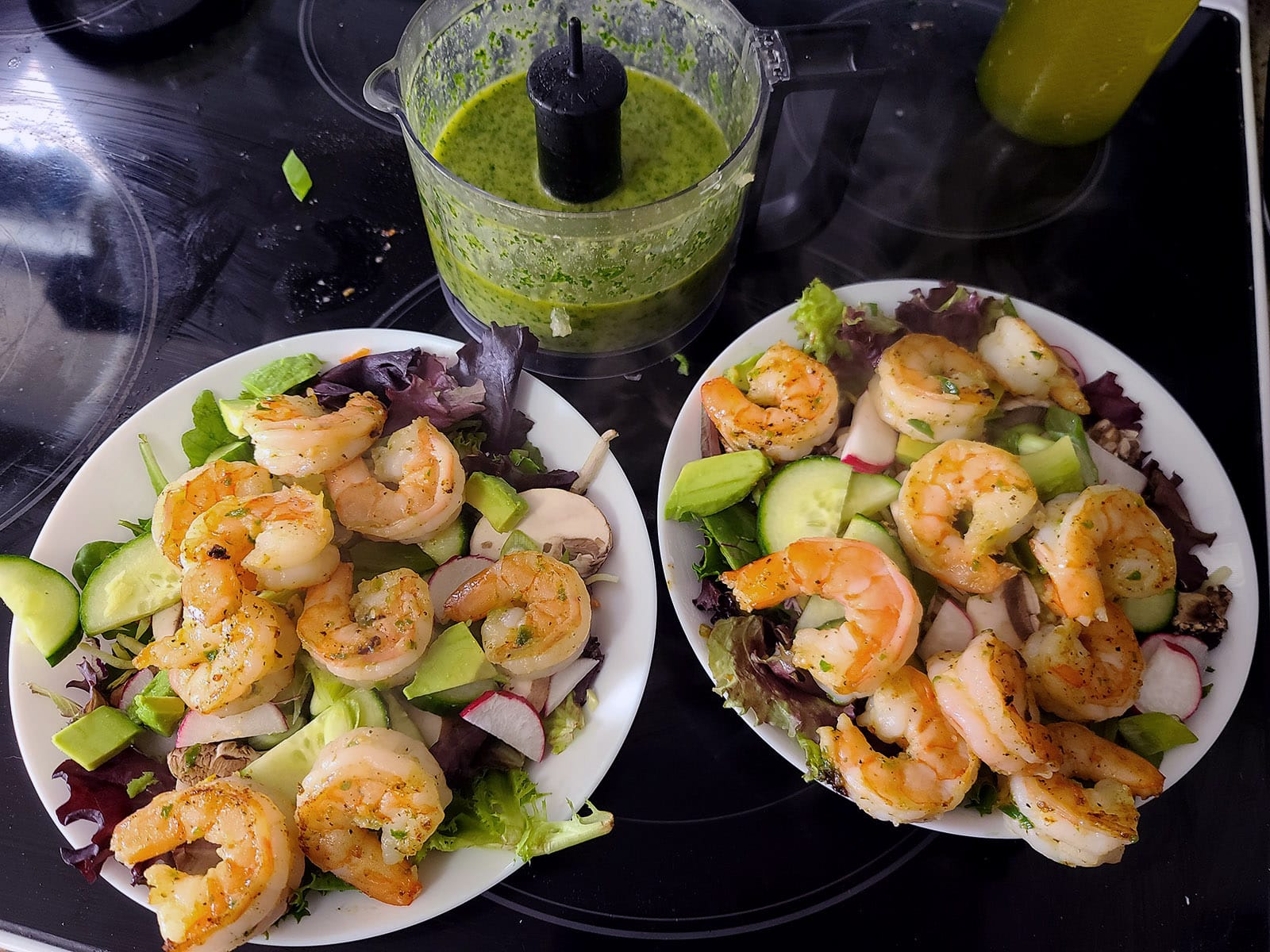 Two bowls of salad with shrimp on them, in front of a mini food processor of cilantro lime dressing.