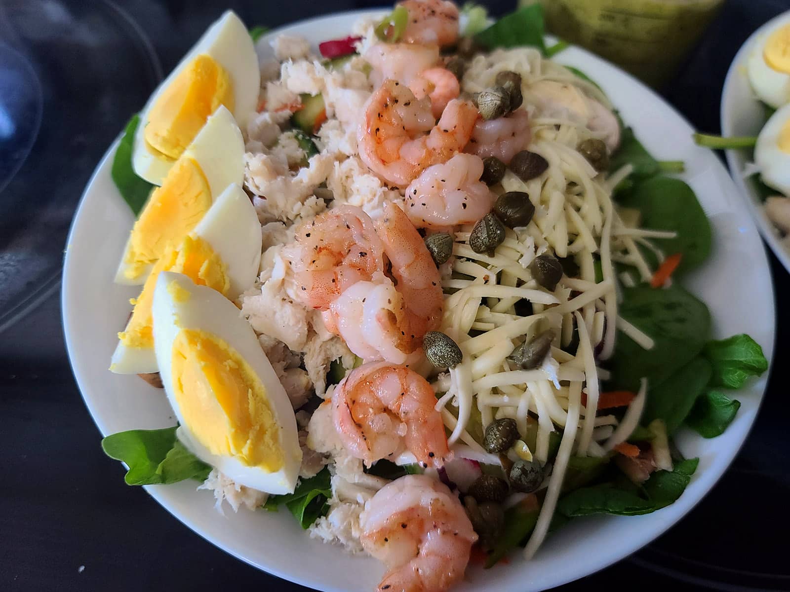 A bowl of seafood cobb salad with shrimp, canned crab, and boiled eggs on it.