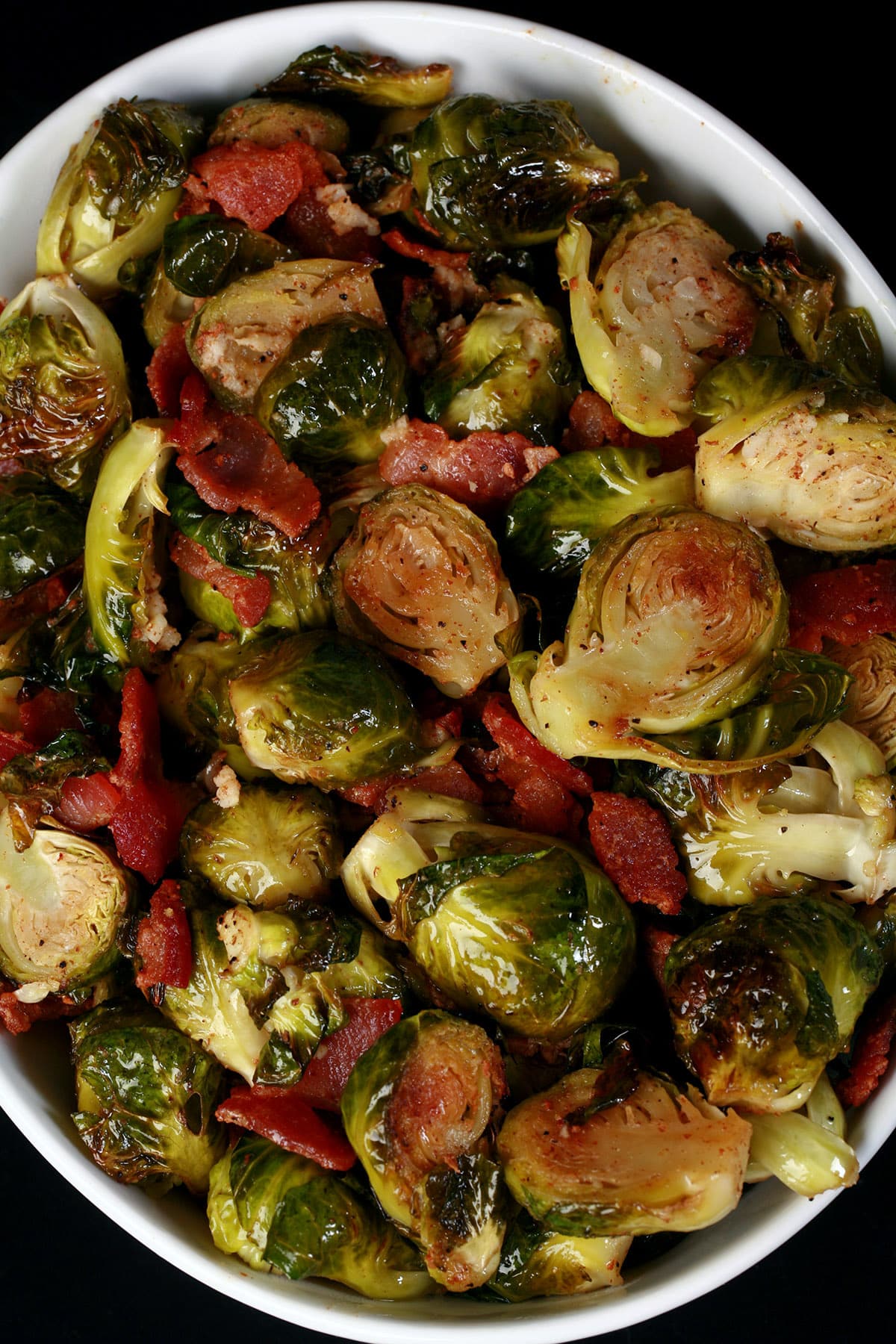 A large white bowl of roasted kero brussels sprouts with bacon and vinaigrette.