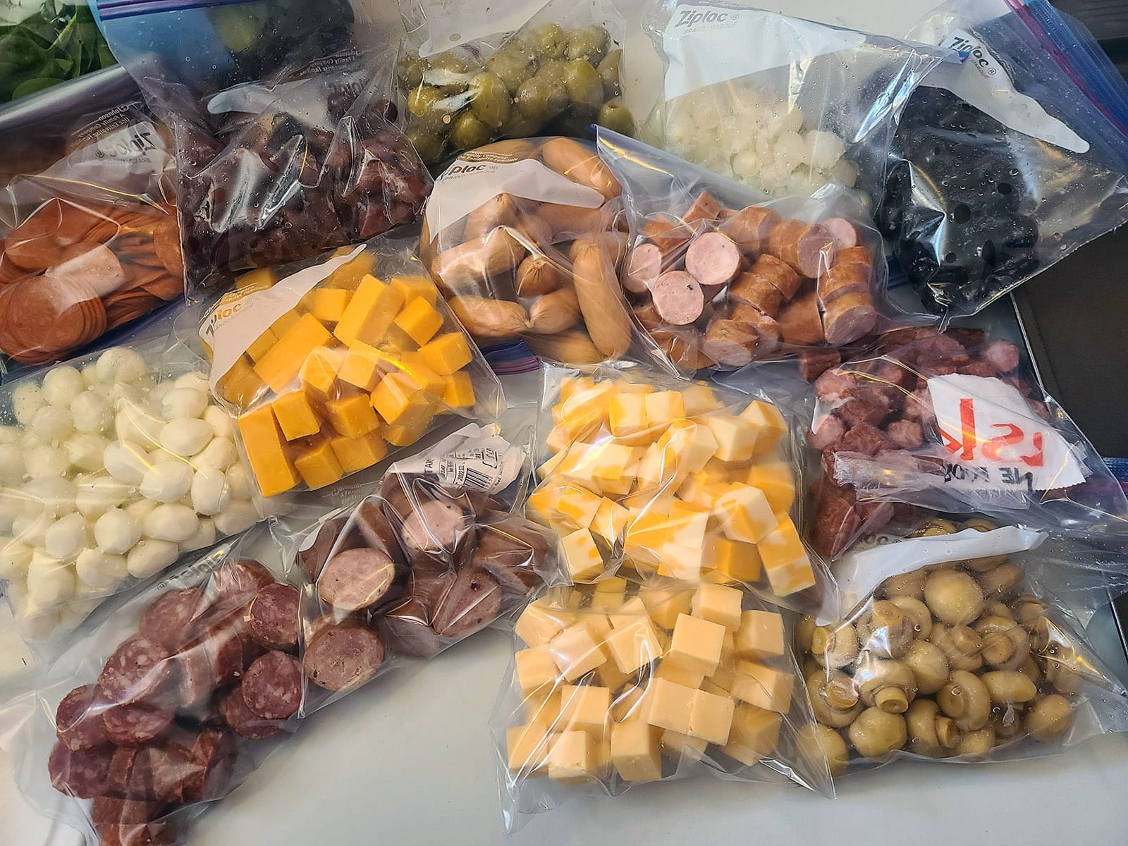 Several bags of cheeses, meats, and olives in a pile.