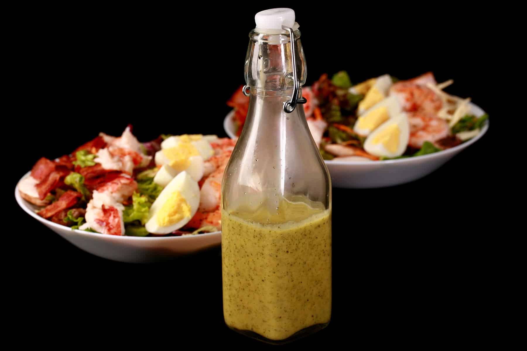 A bottle of lemon dill vinaigette in front of a seafood cobb salad.