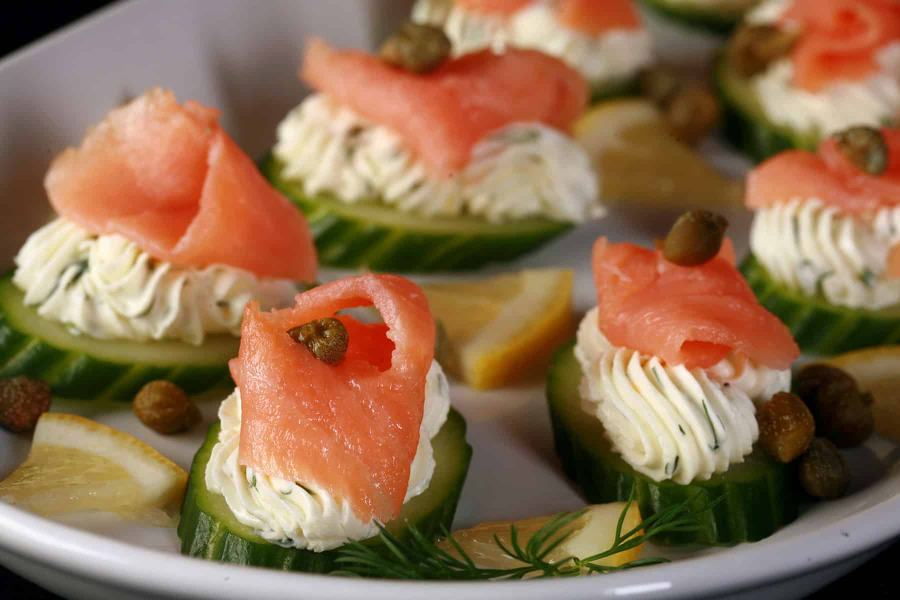 A plate of keto smoked salmon canapes with piped flavoured cream cheese on cucumber slices.