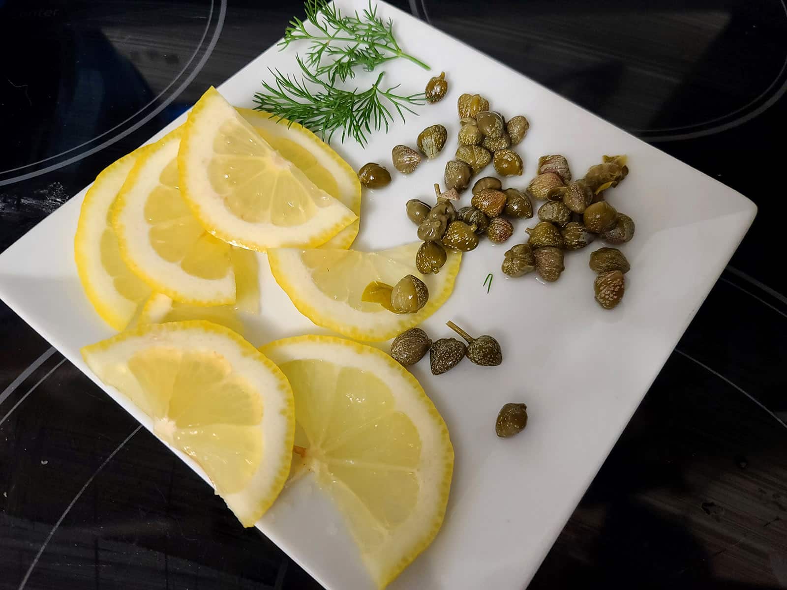 A plate of baby dill, lemon slices, and capers, for garnish.