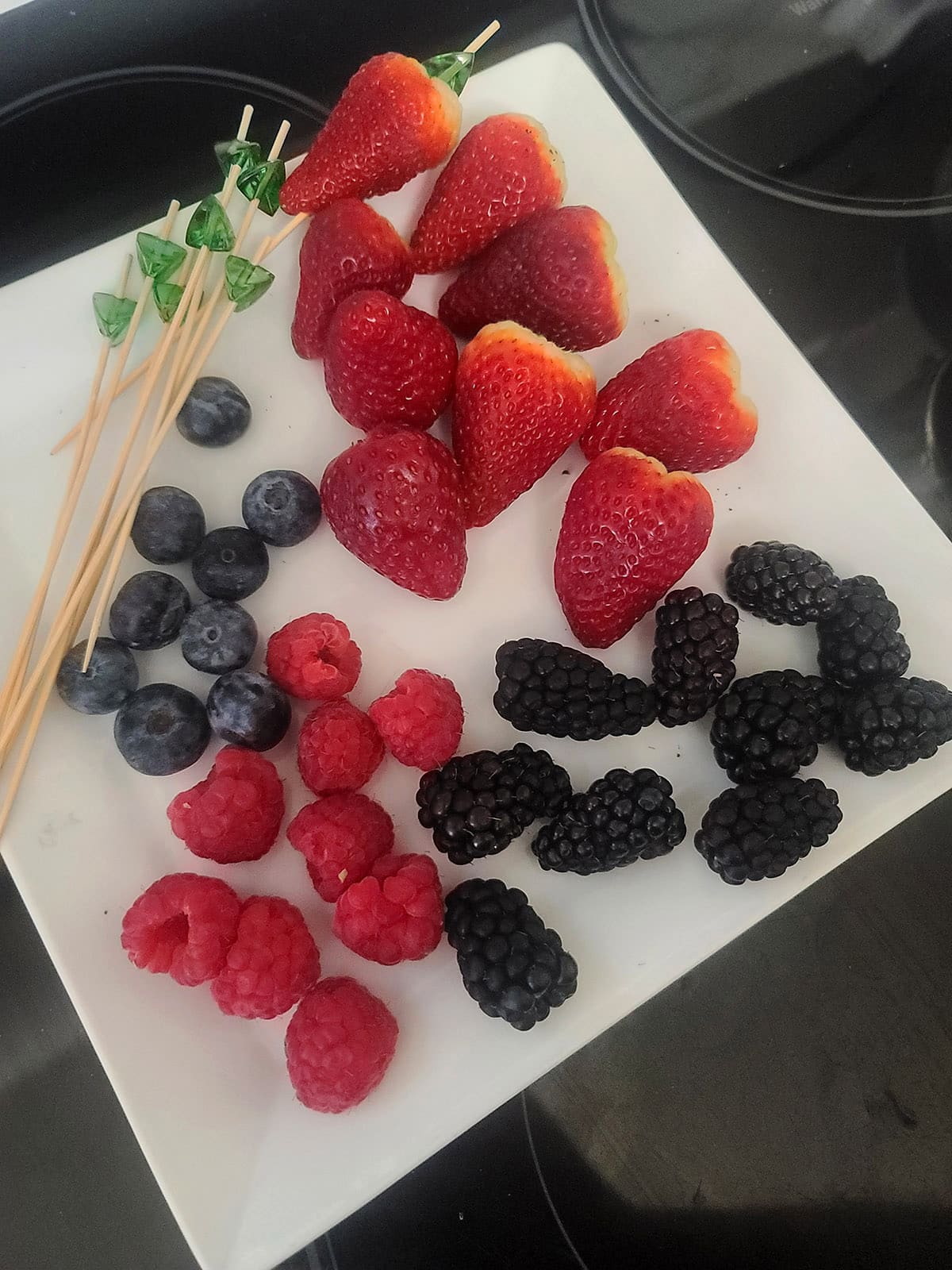 Berries and bamboo skewers laid out on a plate.