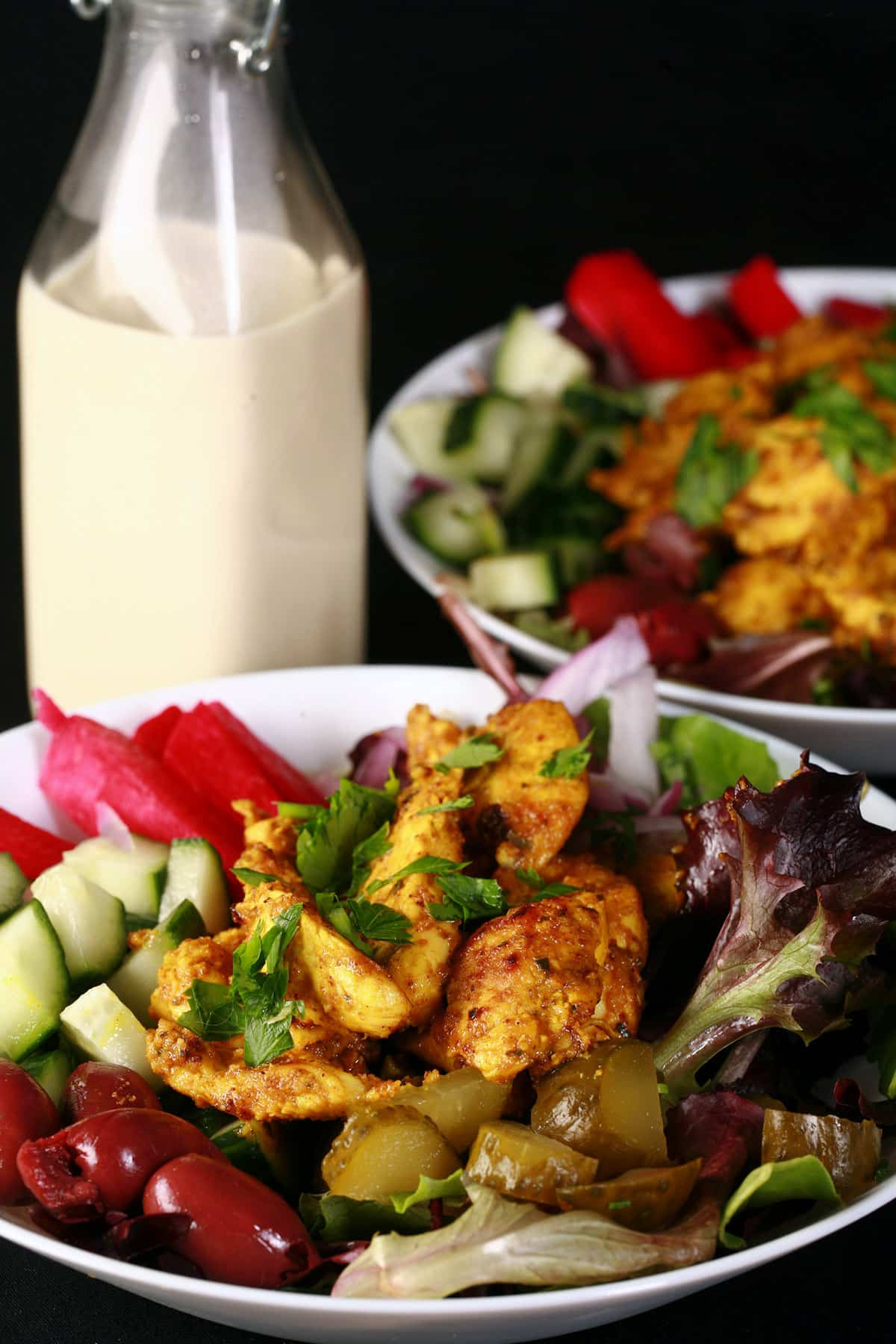 Two chicken shawarma salads with a bottle of garlic tahini dressing,