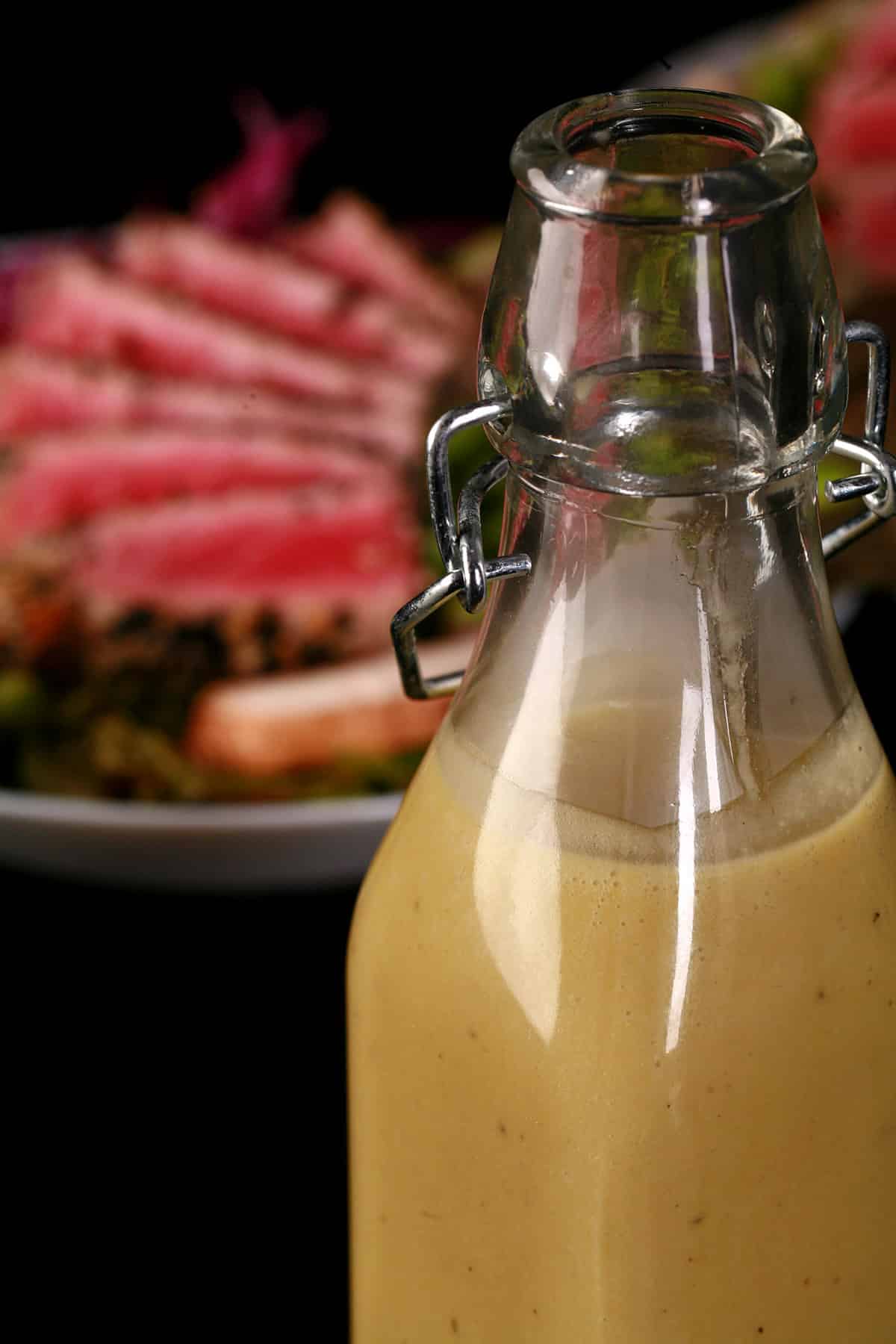 A bottle of creamy wasabi dressing in front of a seared tuna salad.