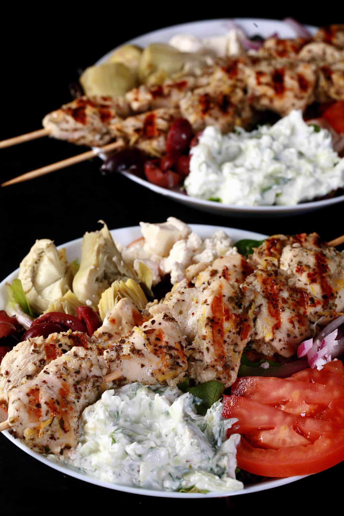 2 bowls of mediterranean chicken salad with chicken souvlaki on top.