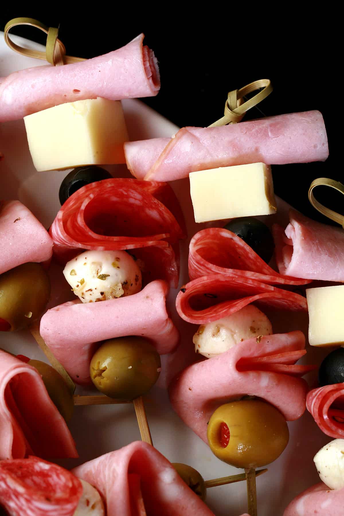 A tray of prepared muffaletta skewers, each with meats, cheeses, and olives.