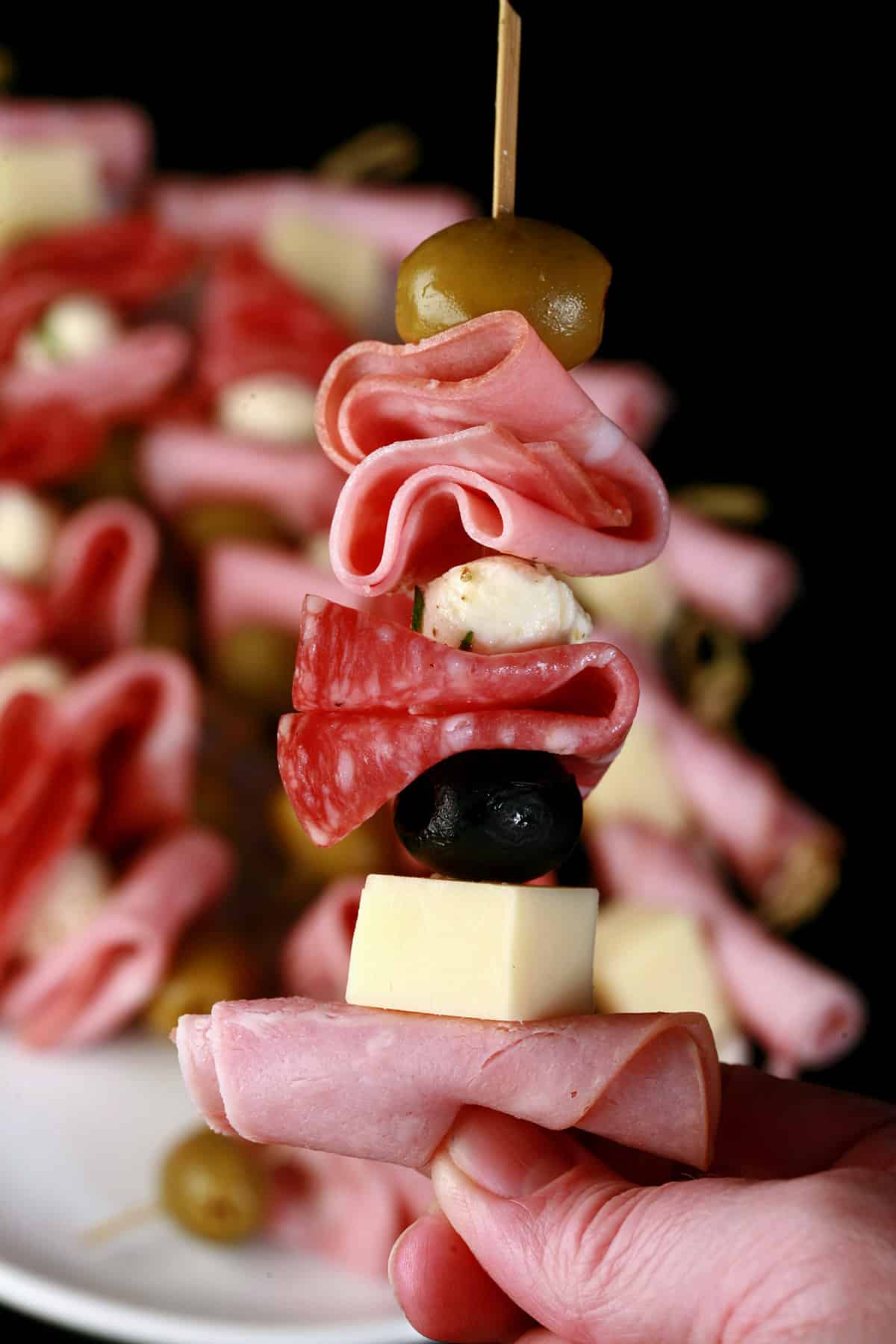 A tray of prepared muffaletta skewers, each with meats, cheeses, and olives.