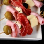 A tray of prepared muffaletta skewers, each with meats, cheeses, and olives.