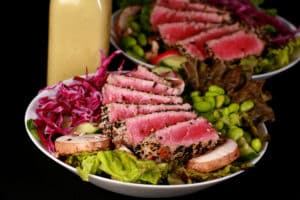 A seared tuna salad with a bottle of creamy wasabi dressing behind it.