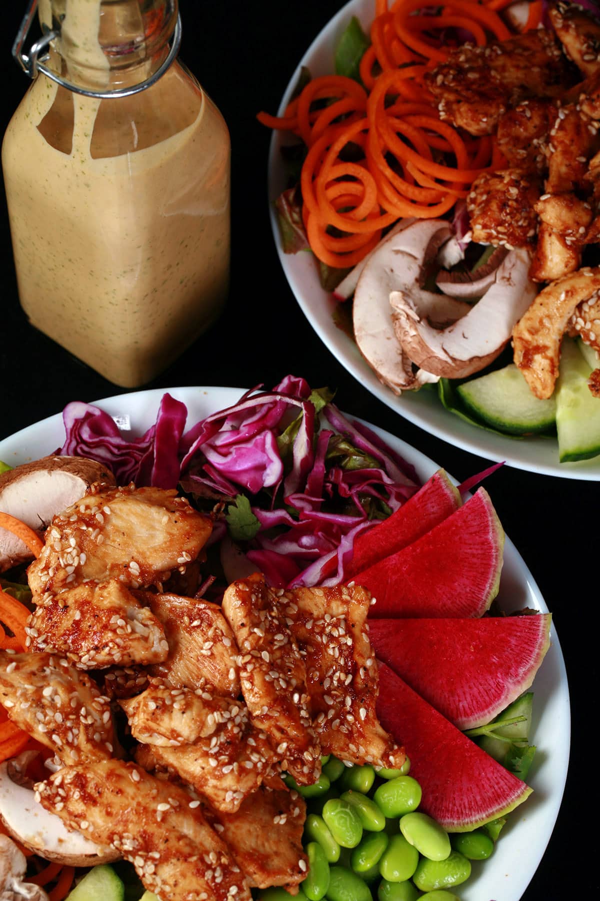 2 bowls of sesame ginger chicken salad with a bottle of peanut dressing behind them.