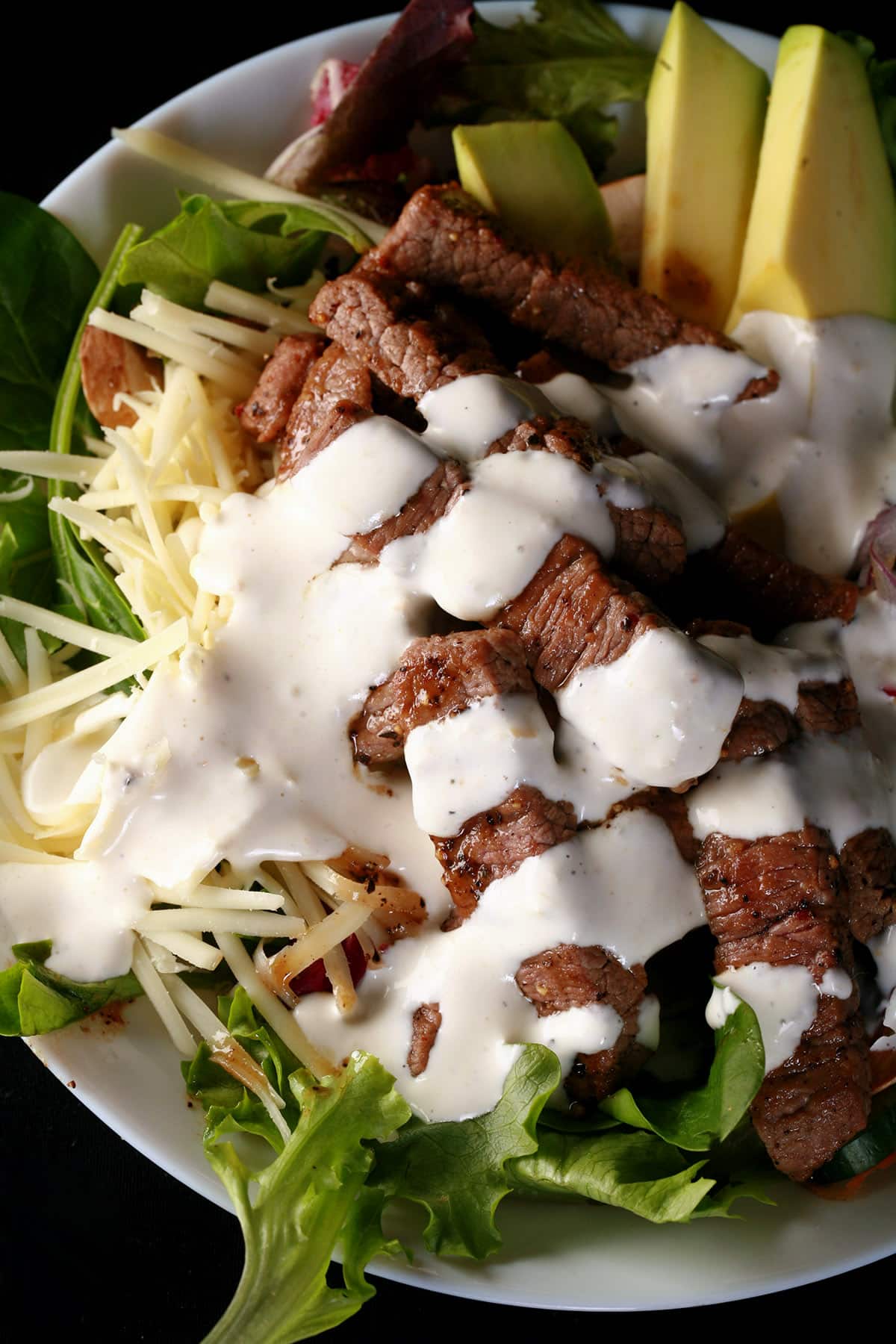 A bowl of steak salad with horseradish dressing drizzled over it.