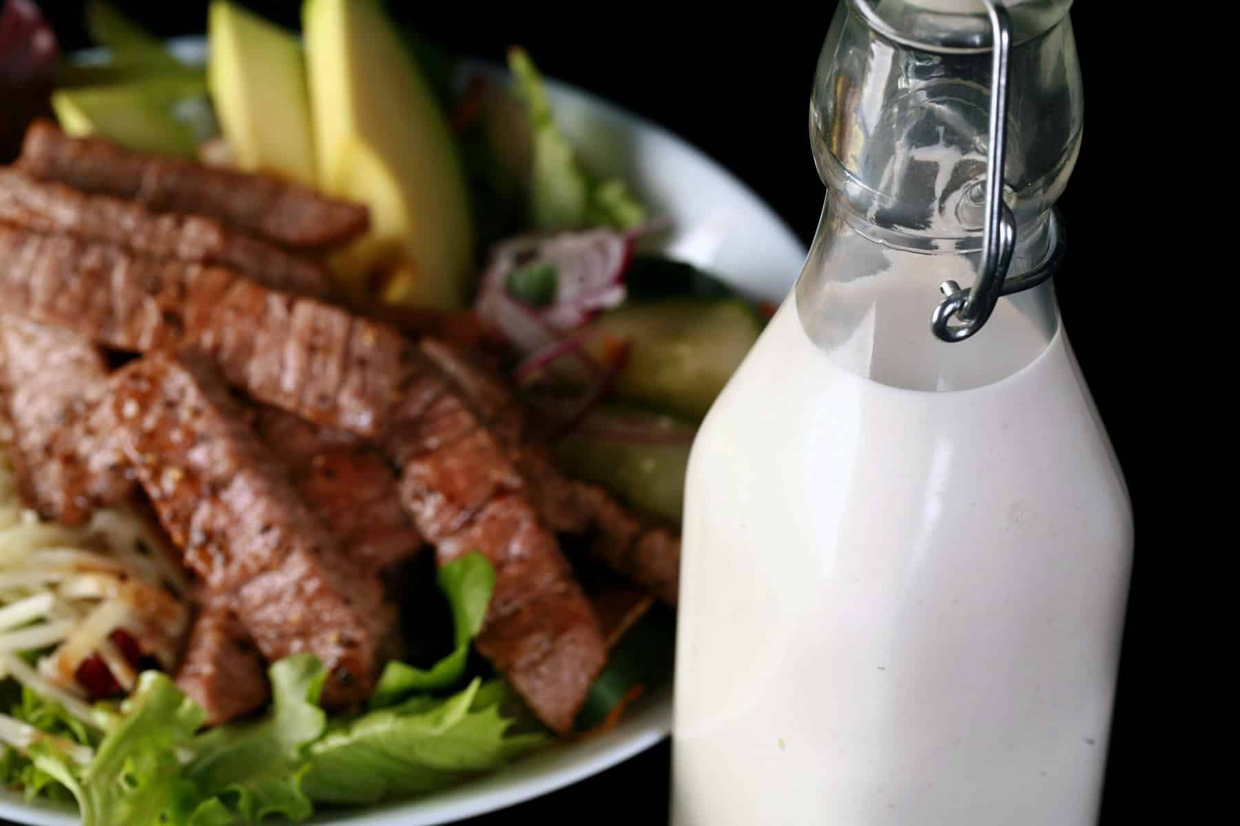 A bowl of steak salad with a jar of creamy horseradish dressing in front of it.