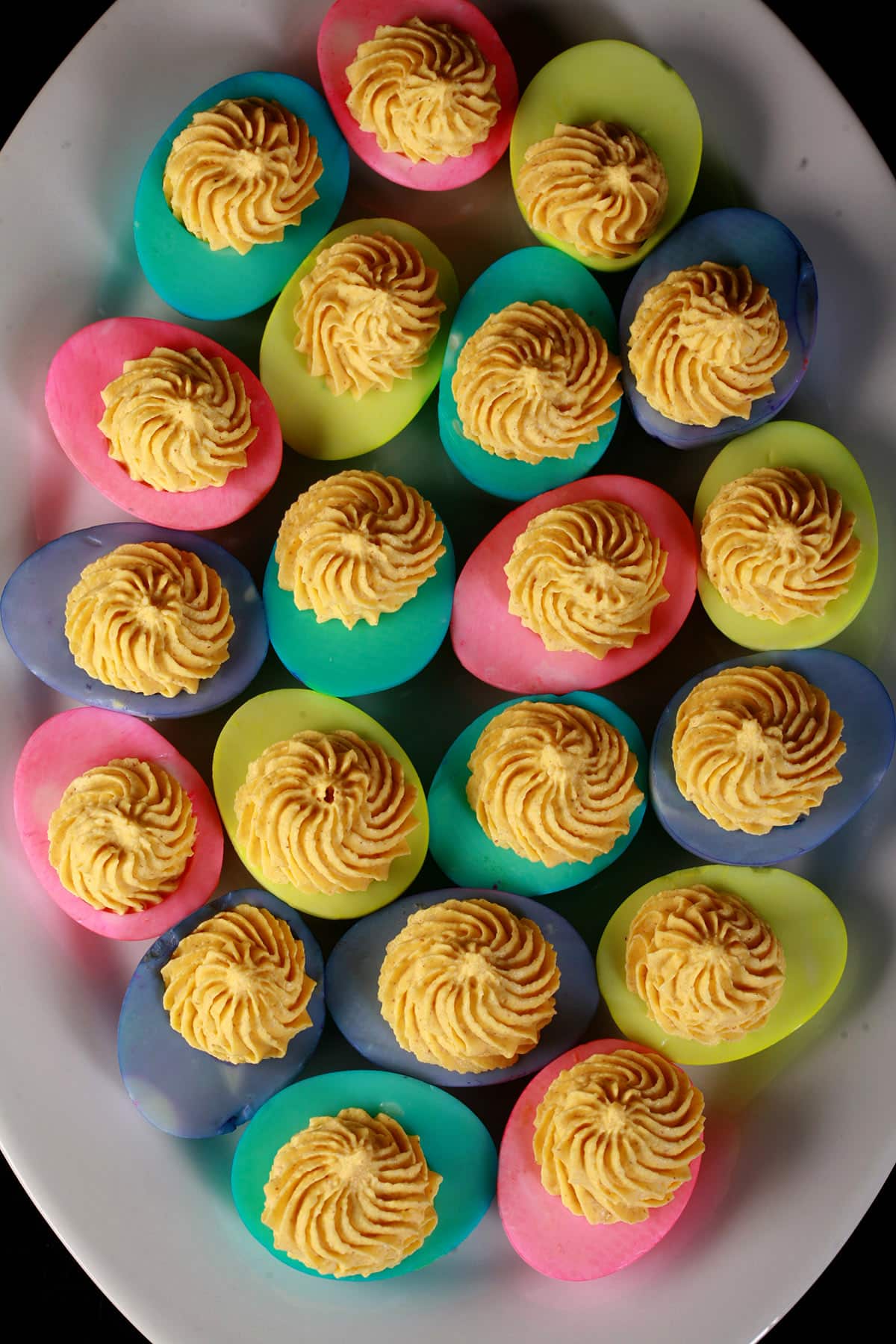 A serving plate of Easter Deviled eggs - yellow yolk mixture piped in swirls onto multicolored egg whites.