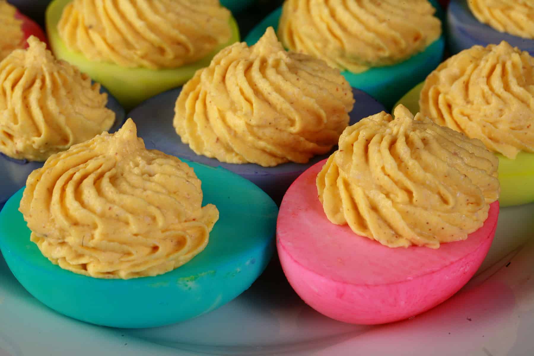 A serving plate of colored deviled eggs, where the whites have been dyed hot pink, lime green, turquoise, and light purple.