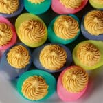 A serving plate of Easter Deviled eggs - yellow yolk mixture piped in swirls onto multicolored egg whites.