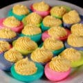 A serving plate of colored deviled eggs, where the whites have been dyed hot pink, lime green, turquoise, and light purple.