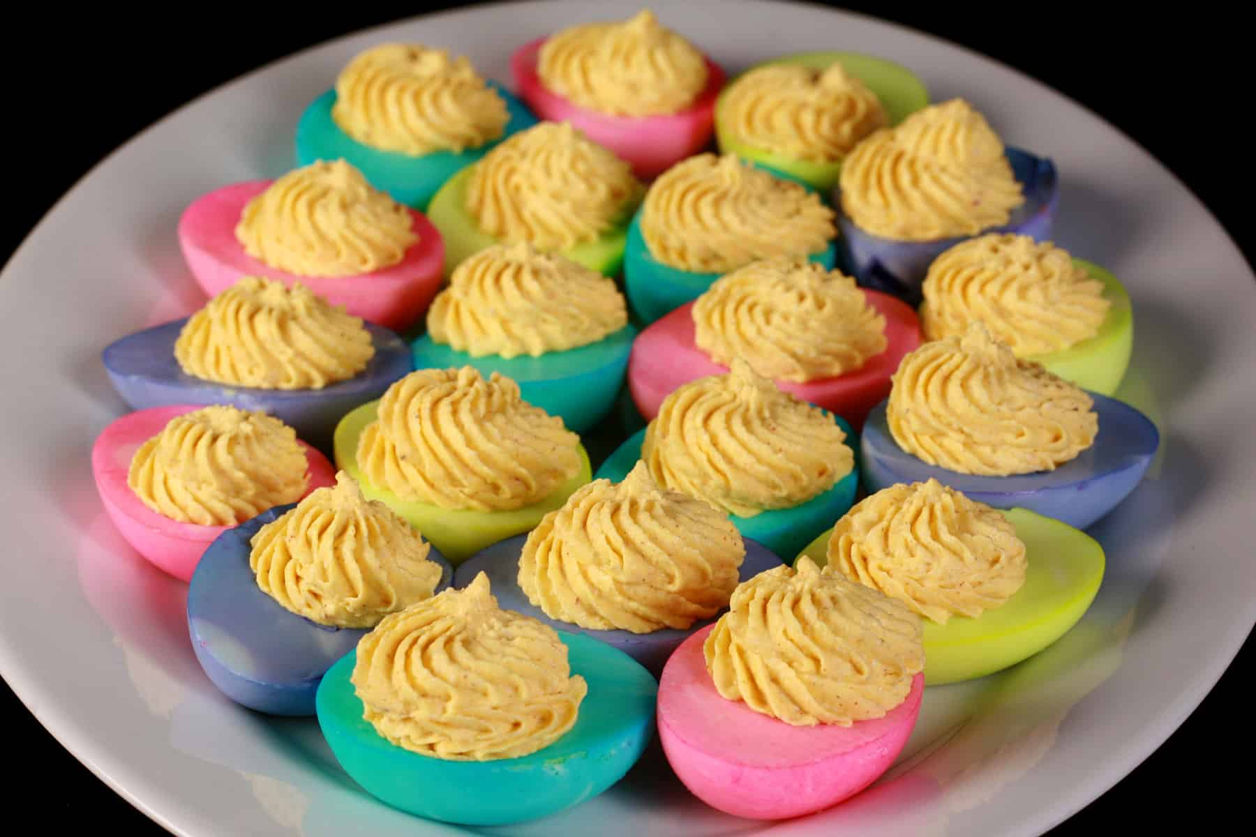 A serving plate of colored deviled eggs, where the whites have been dyed hot pink, lime green, turquoise, and light purple.