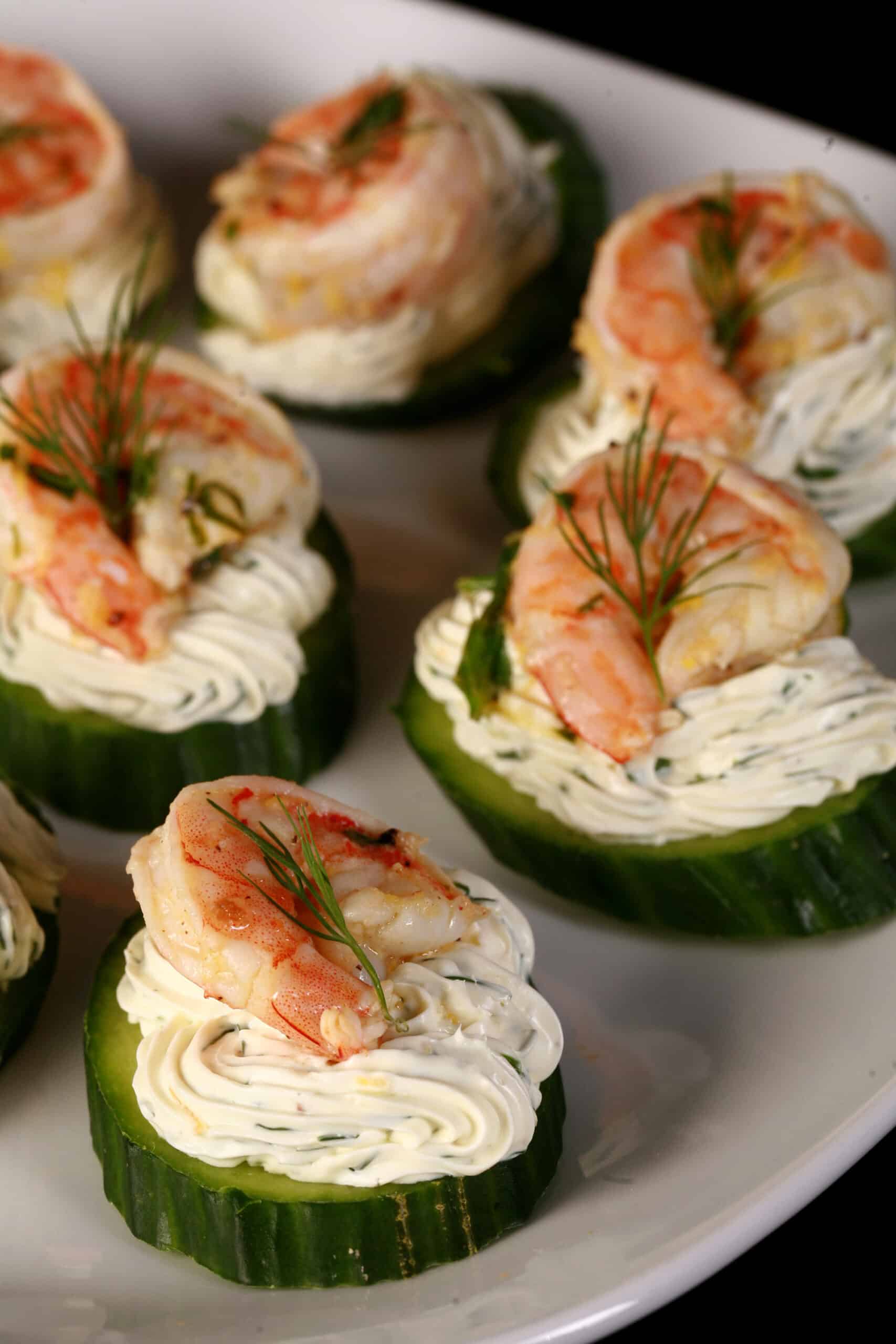 A plate of cucumber canapes, topped with herb cream cheese, shrimp, and dill.