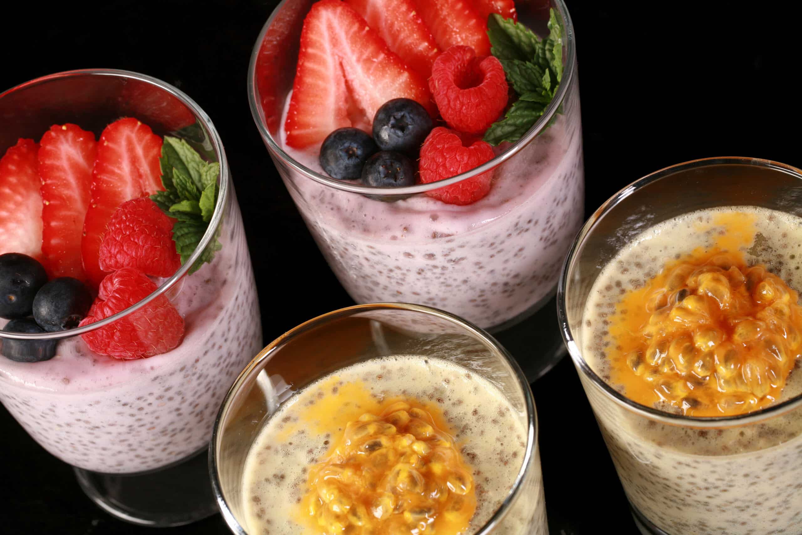 4 glasses of keto protein pudding with chia seeds.  2 are yellow and topped with passionfruit, the other two are pink and topped with berries.