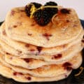 A stack of 6 blackberry protein pancakes with blackberries and lemon curls on top.