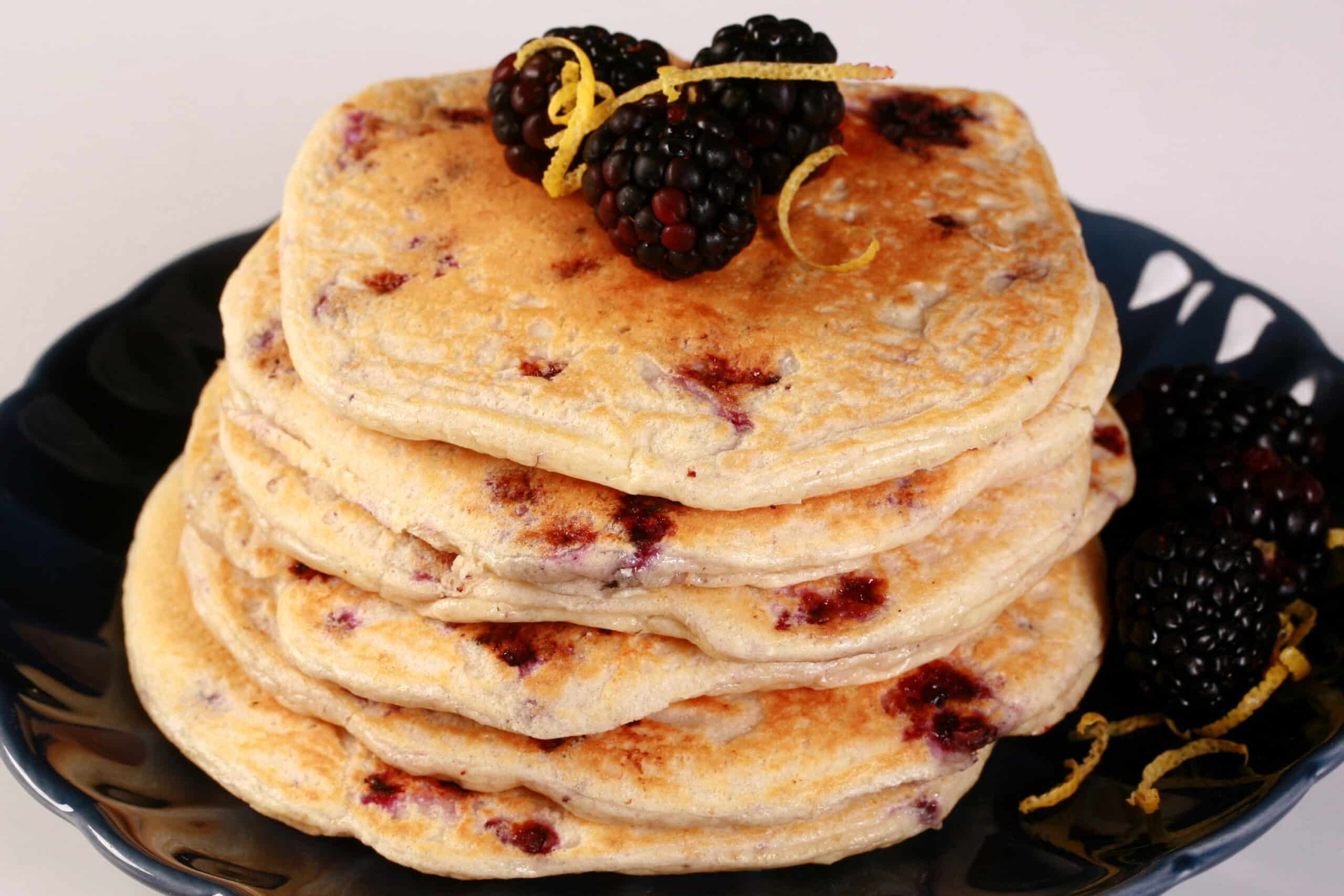 A stack of 6 blackberry protein pancakes with blackberries and lemon curls on top.