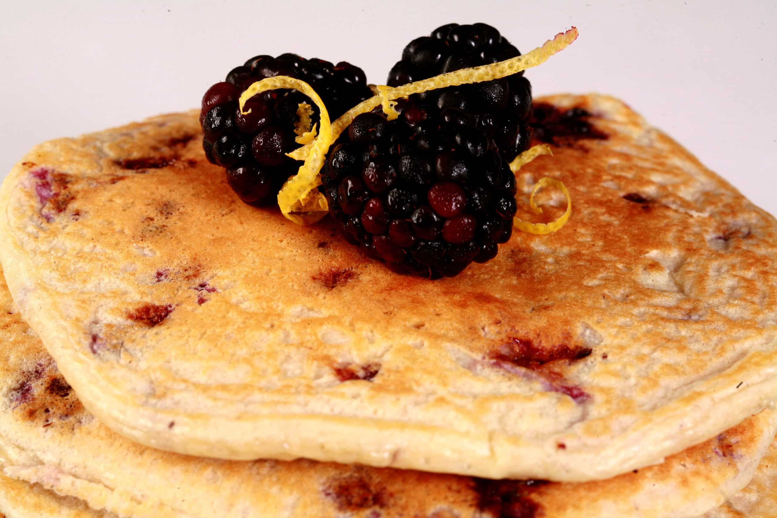 A stack of 6 keto blackberry pancakes with blackberries and lemon curls on top.