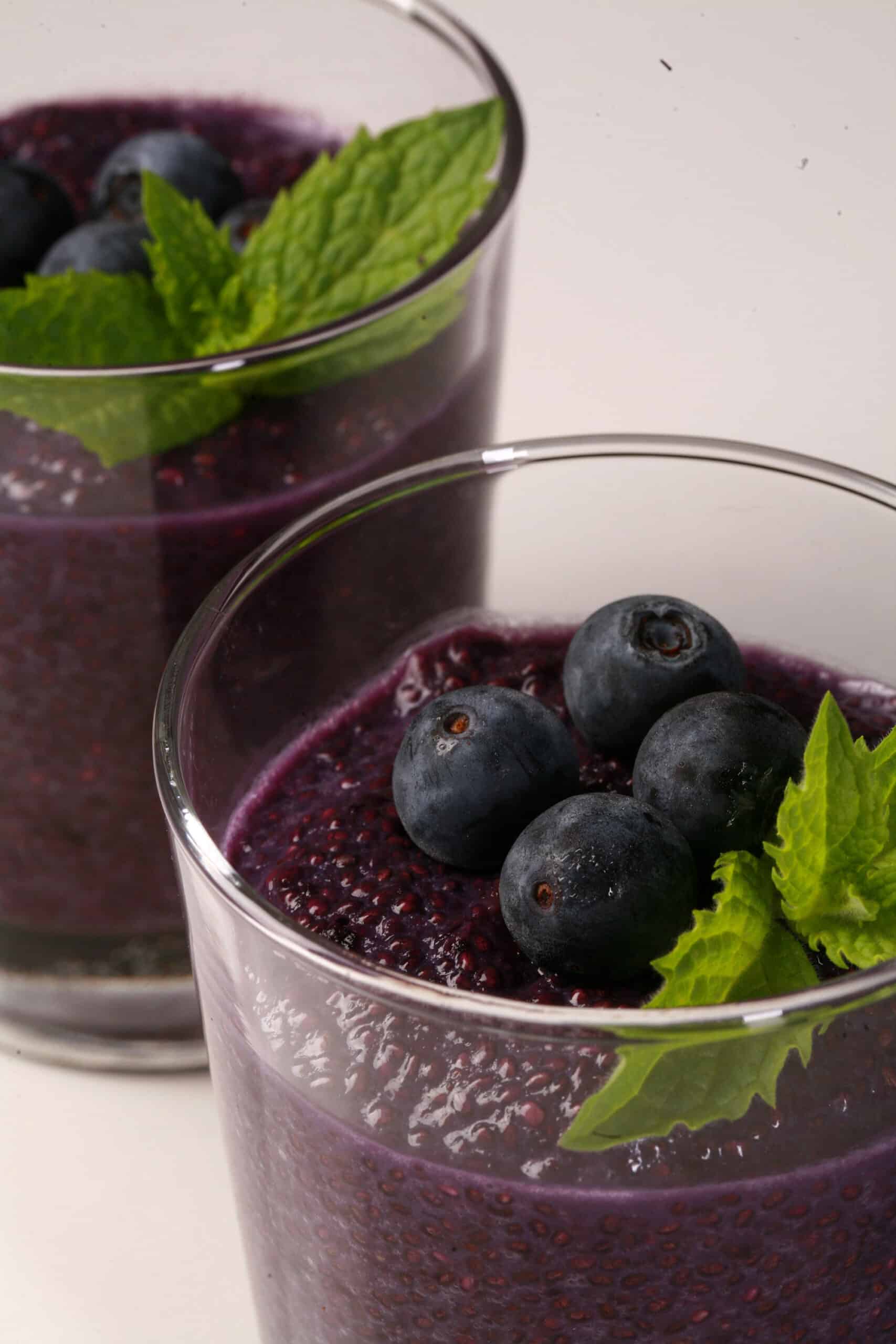 2 glasses of blueberry chia pudding, topped with fresh blueberries and a mint sprig.