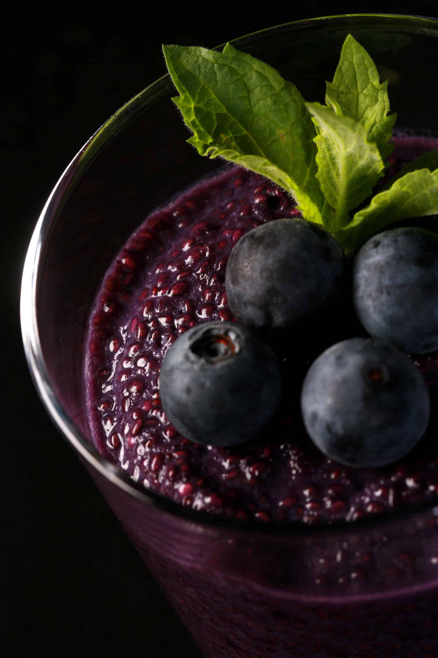 2 glasses of blueberry chia seed pudding, topped with fresh blueberries and a mint sprig.