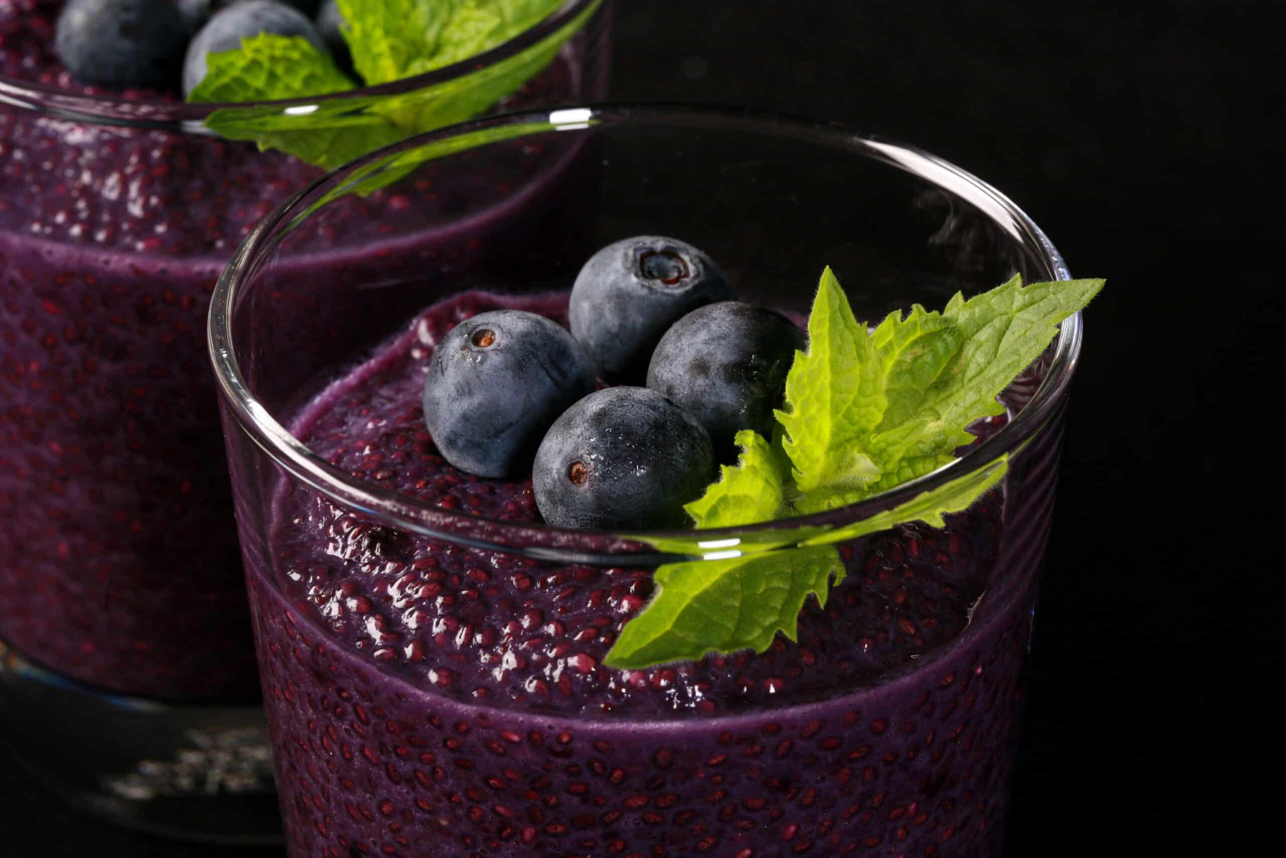 2 glasses of blueberry chia seed pudding, topped with fresh blueberries and a mint sprig.