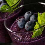 2 glasses of blueberry chia pudding, topped with fresh blueberries and a mint sprig.