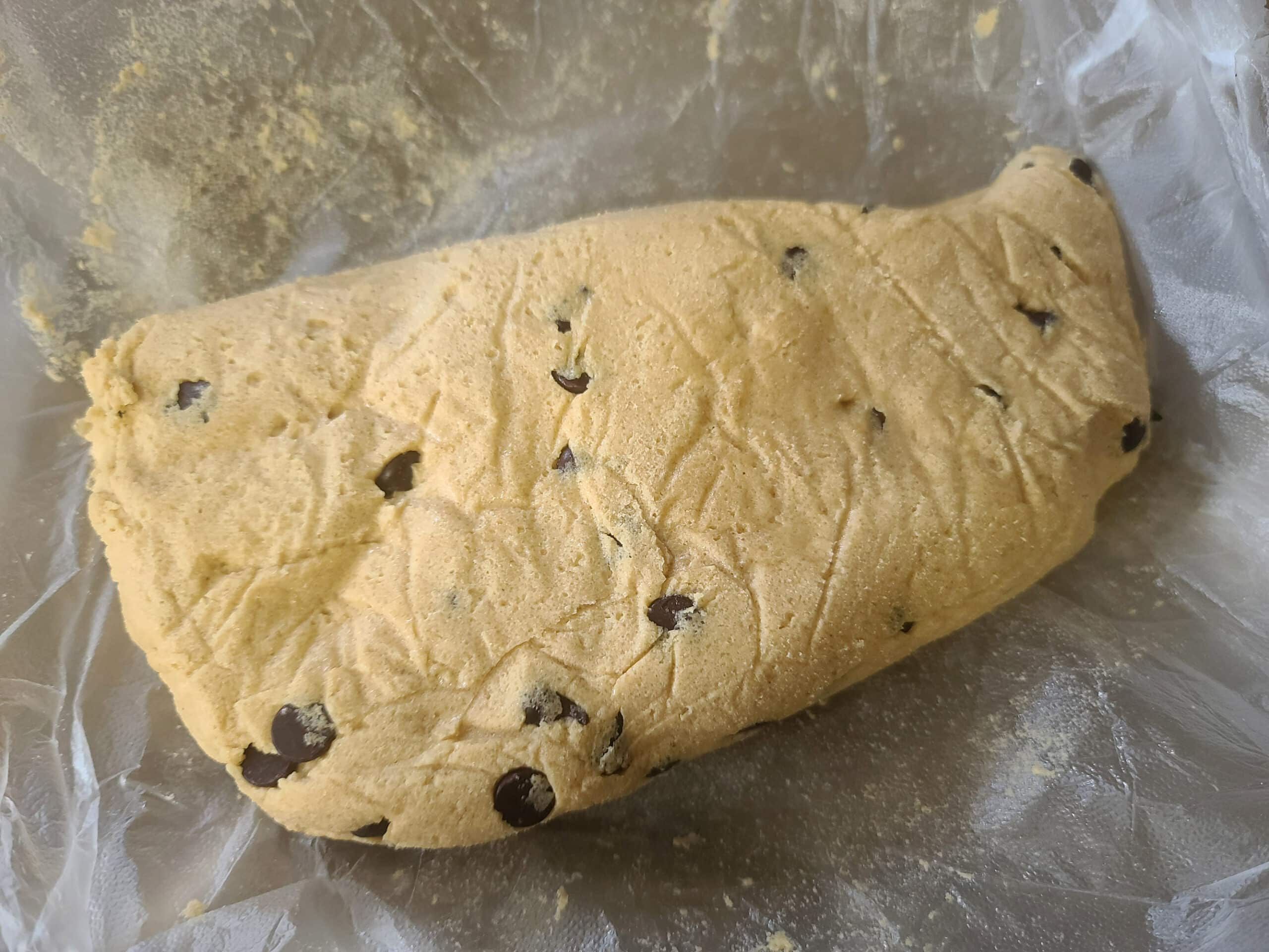 A chunk of chilled keto peanut butter chocolate chip cookie dough, on plastic wrap.