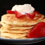 A stack of low carb strawberry protein pancakes topped with whipped cream and strawberry slices.