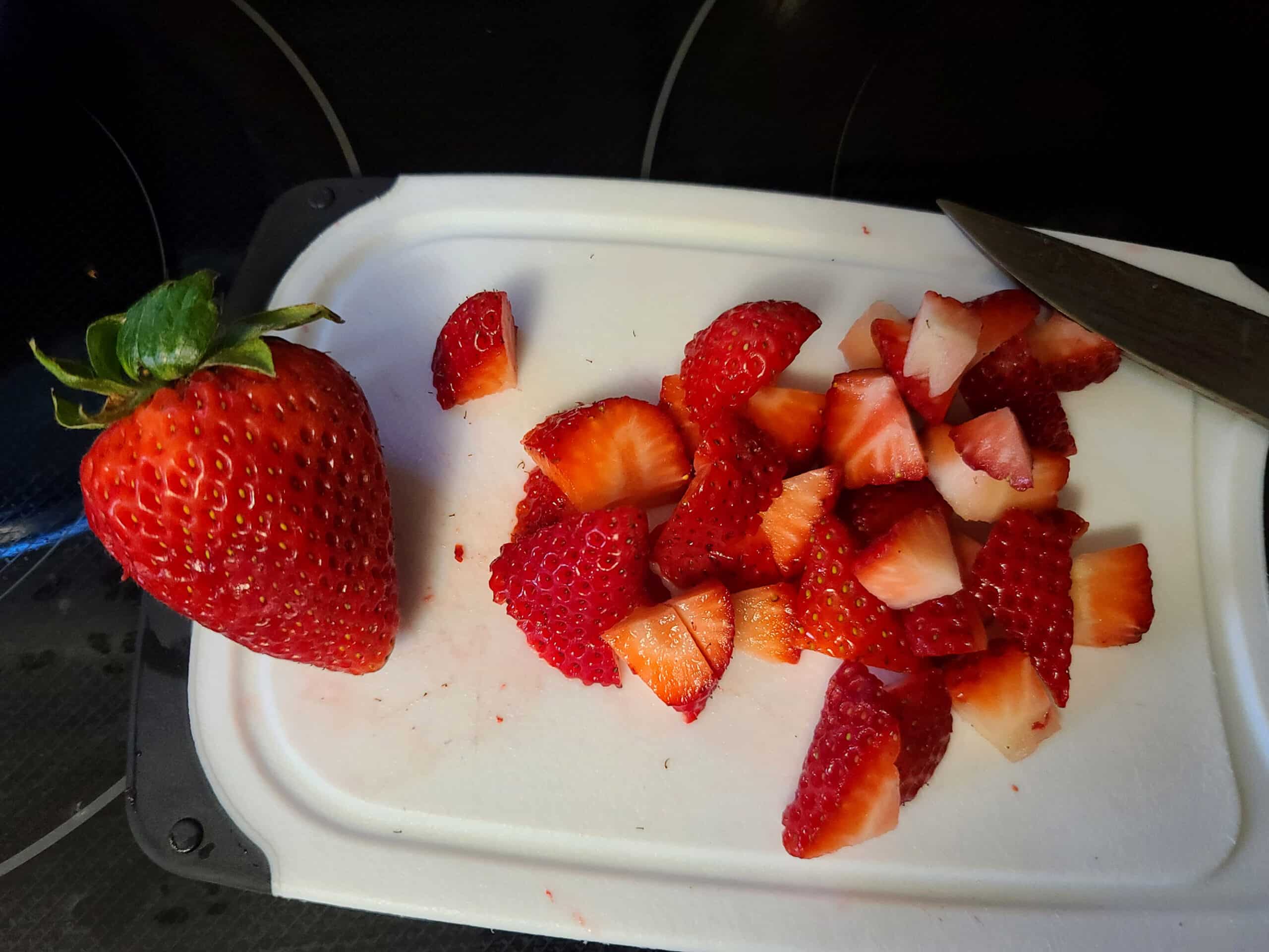 Strawberries being chopped on a white cutting board.