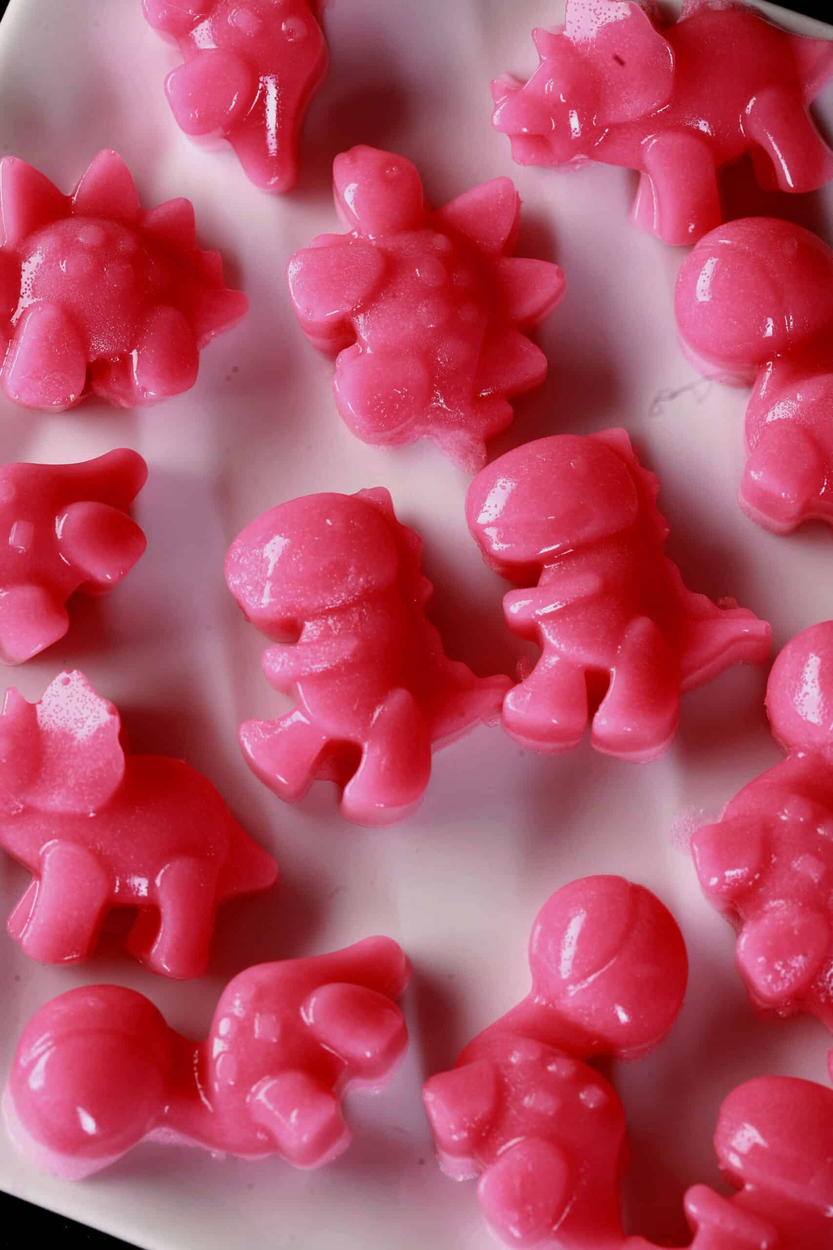Pink dinosaur shaped homemade protein gummies on a plate.