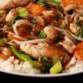 A plate of keto chicken stir fry served over cauliflower rice. Chicken, mushrooms, carrots, peas, and beans sprouts are all visible.