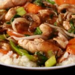 A plate of keto chicken stir fry served over cauliflower rice. Chicken, mushrooms, carrots, peas, and beans sprouts are all visible.