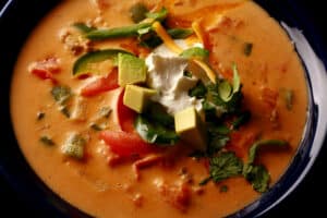 A bowl of cheesy low carb taco soup, garnished with avocado, tomato, cilantro, jalapeno, cheese, and sour cream.