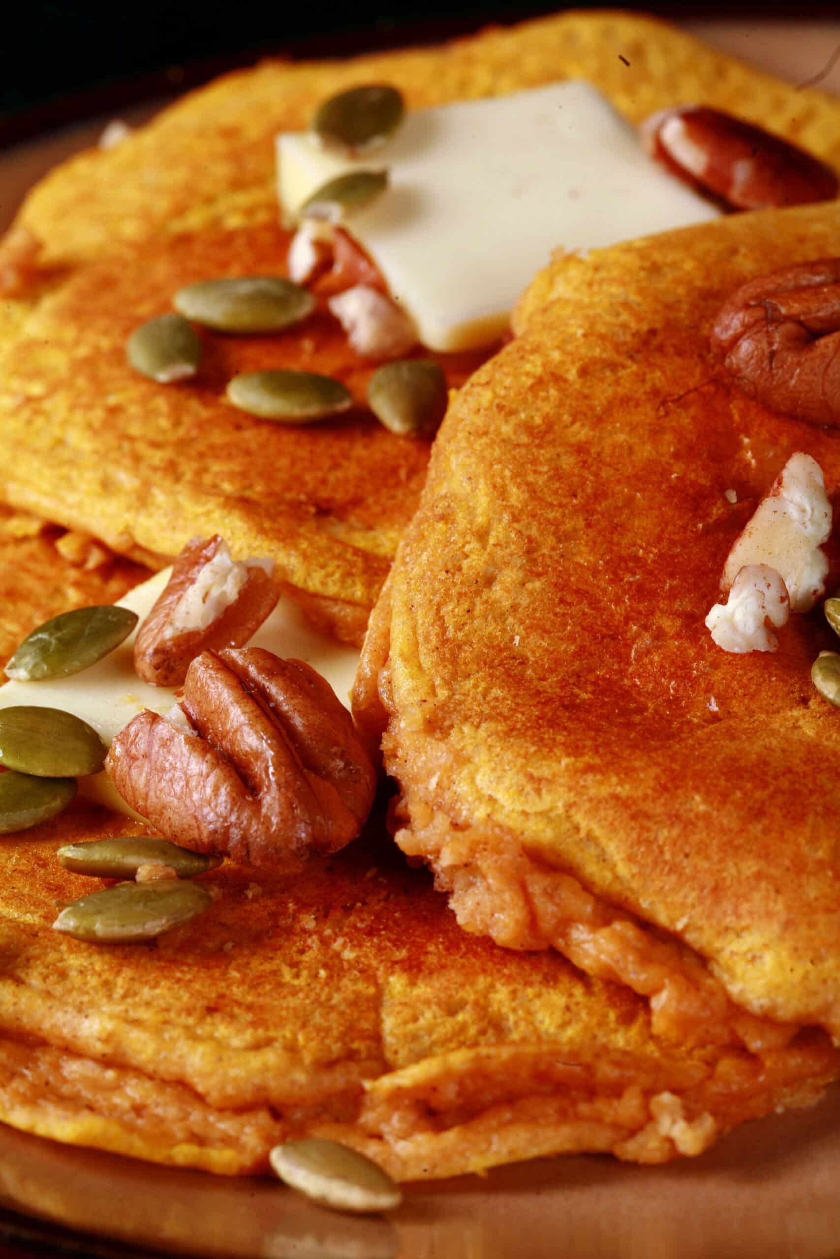 3 low carb pumpkin protein powedr pancakes on a plate, topped with butter, syrup, pecans, and pumpkin seeds.