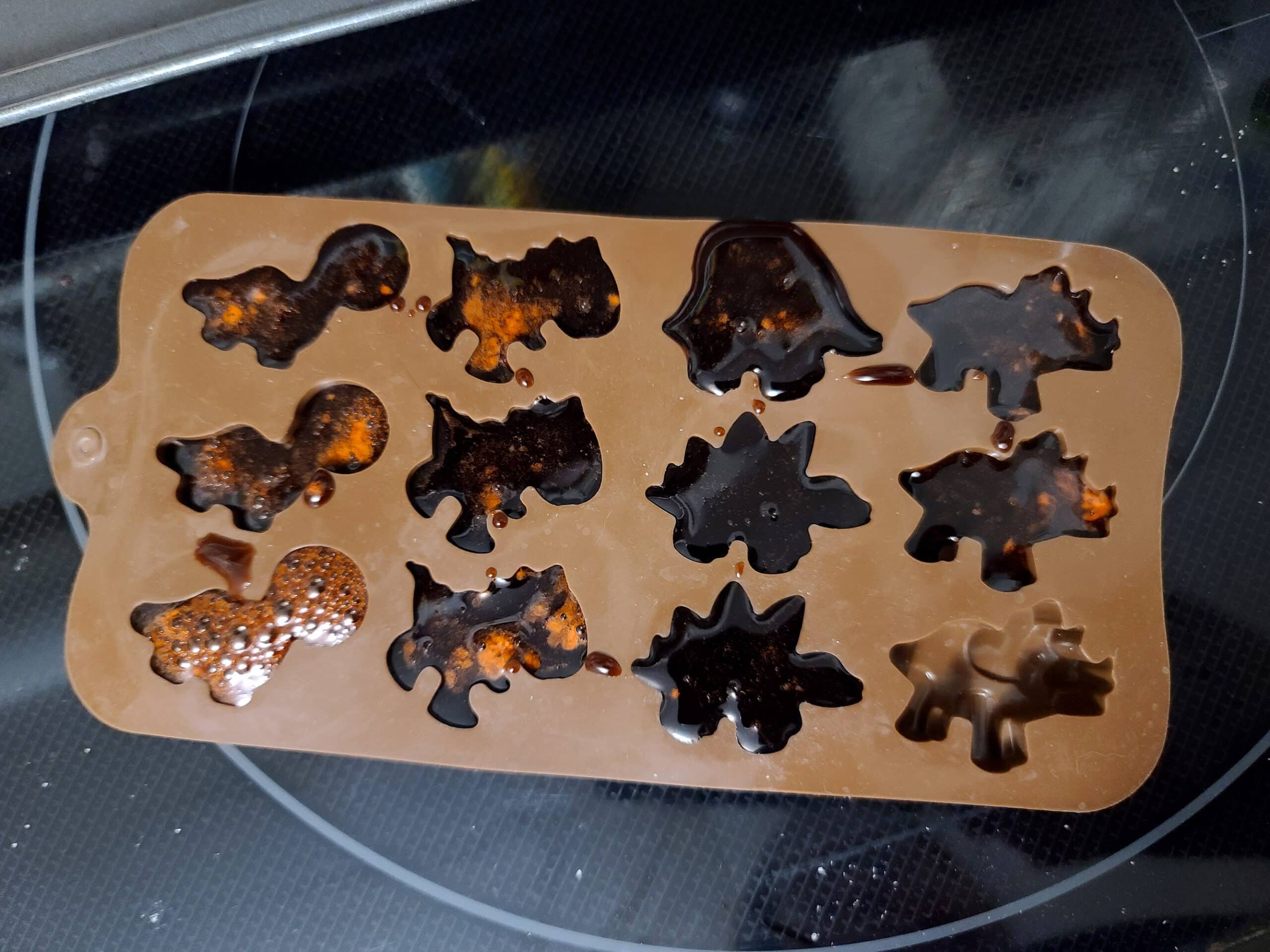 An 8 cavity dinosaur mold, mostly filled with leftover brown gummy liquid.