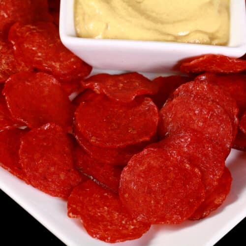 A plate of keto pepperoni chips surrounding a bowl of mustard.