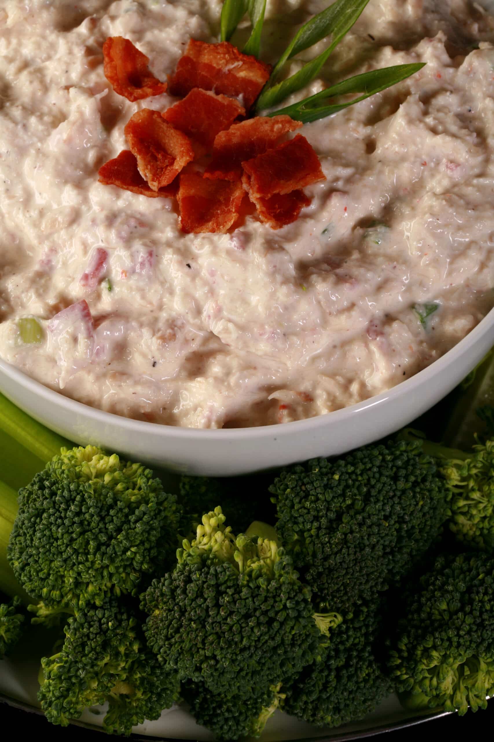 A bowl of smoky keto cold crab dip, topped with bacon and surrounded by vegetables to dip.