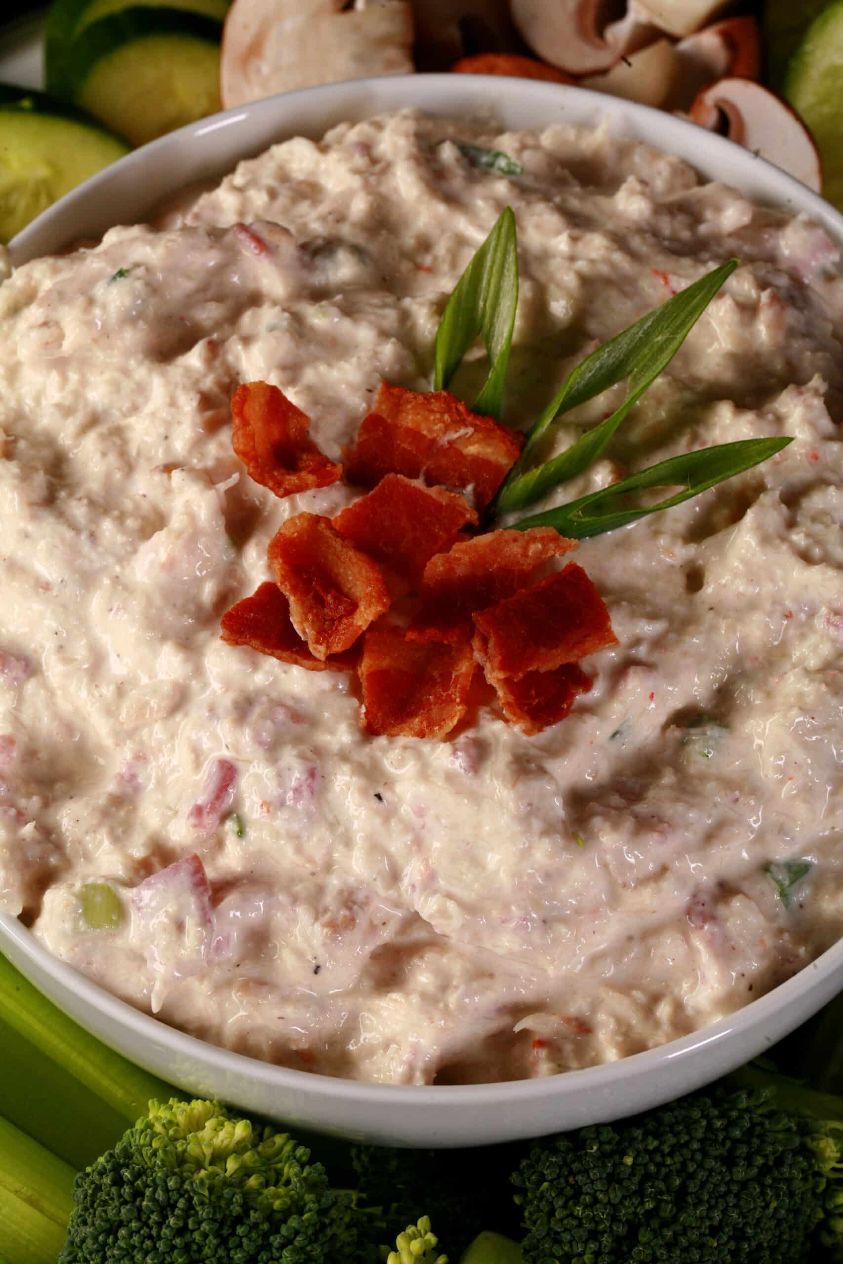 A bowl of smoky keto crab dip, topped with bacon and surrounded by vegetables to dip.