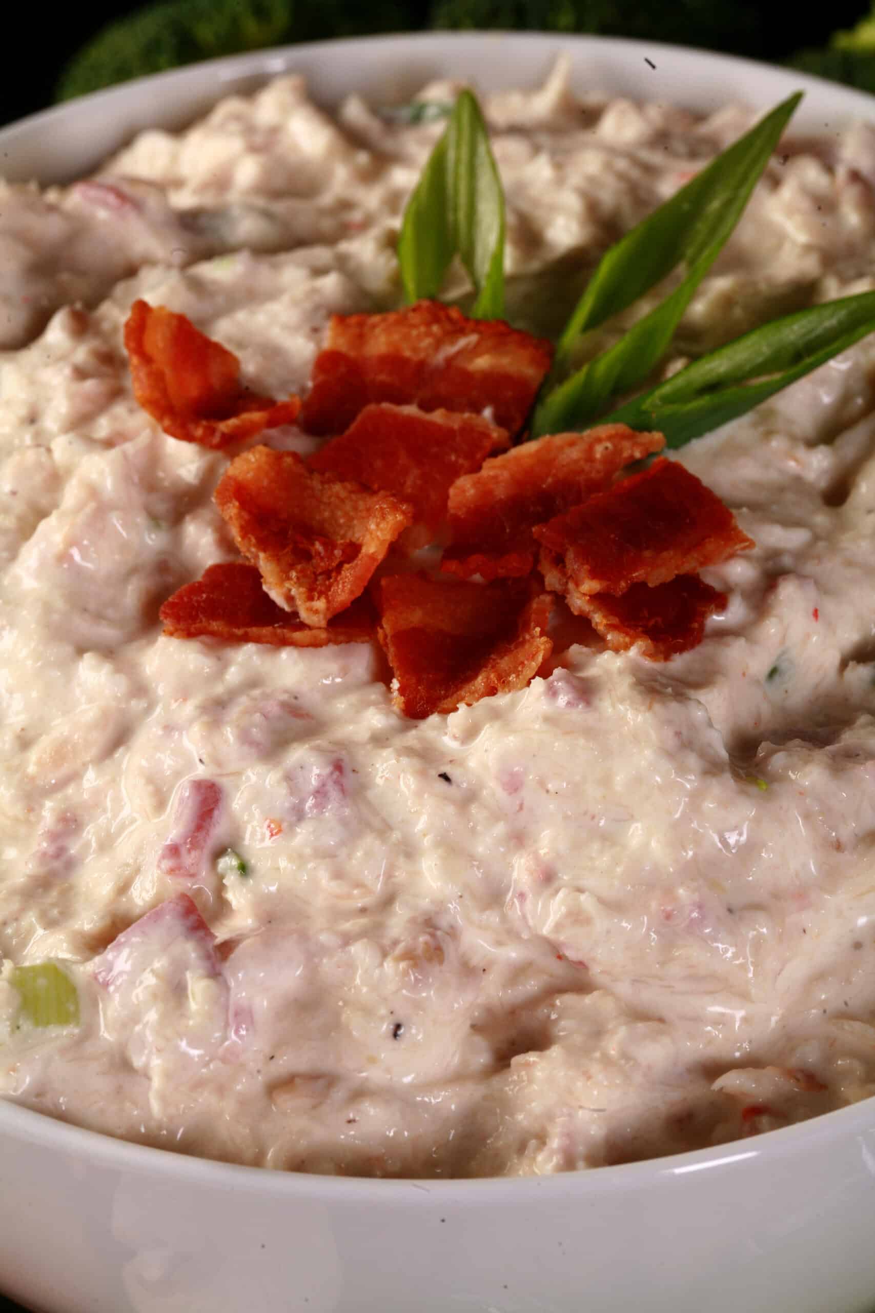 A bowl of smoky low carb crab dip, topped with bacon and surrounded by vegetables to dip.